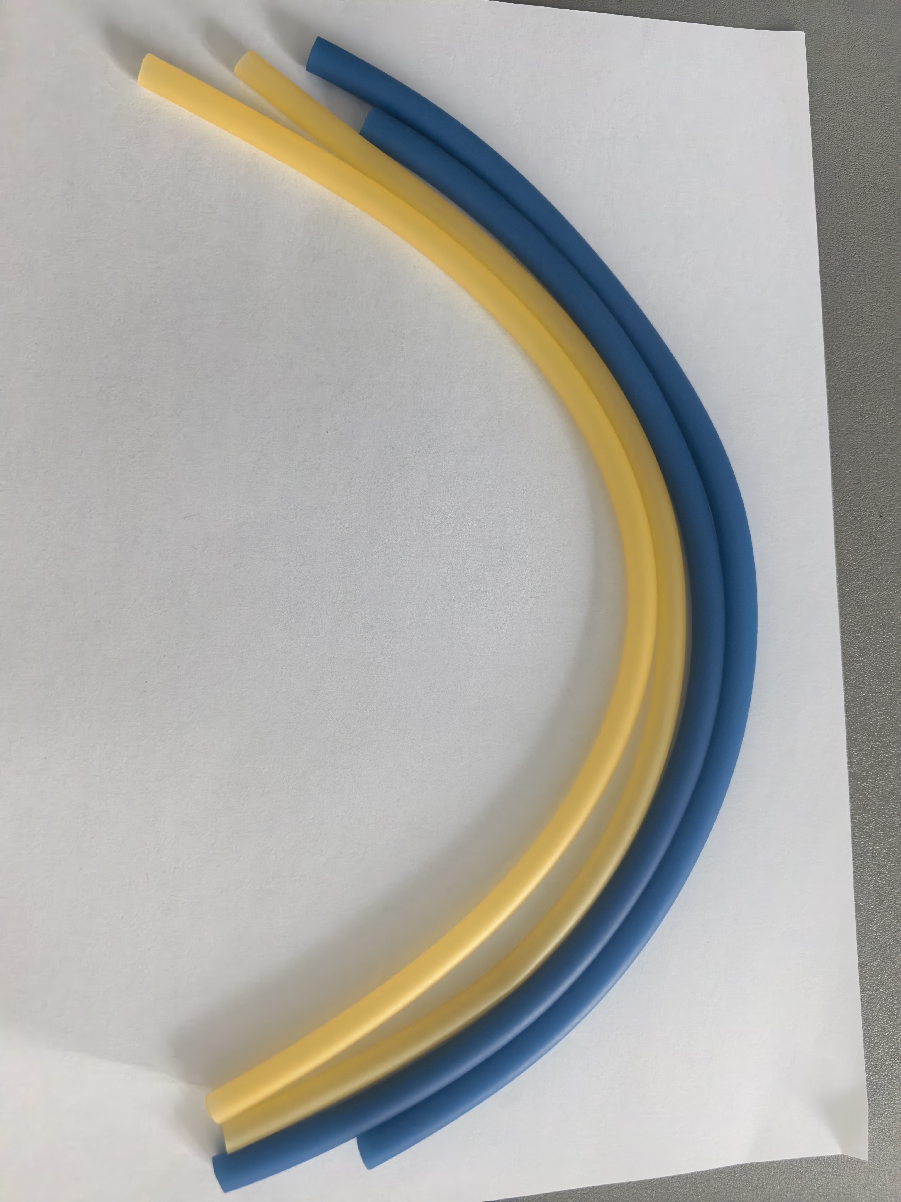 Yellow and blue hemostatic tubes curved side by side on an inspection surface