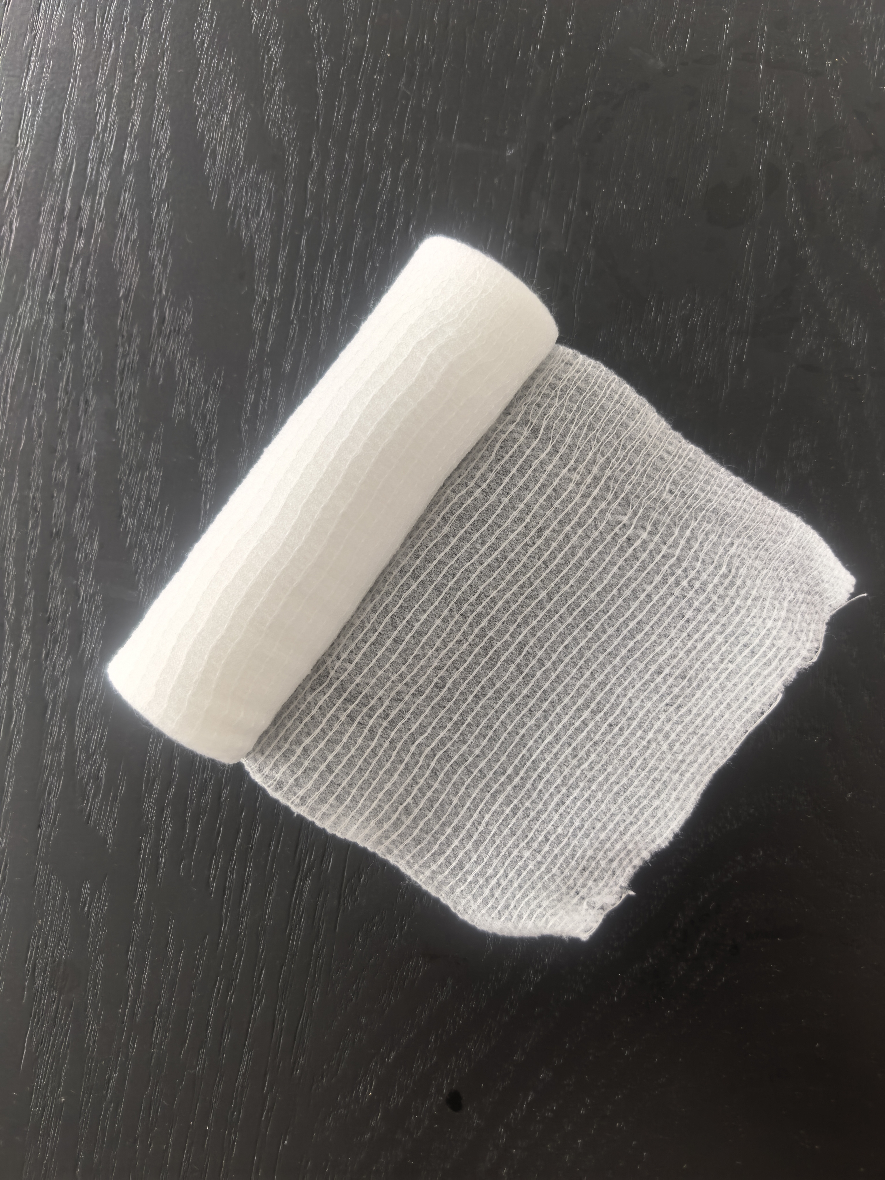 White PBT bandage partly unrolled on a dark inspection surface