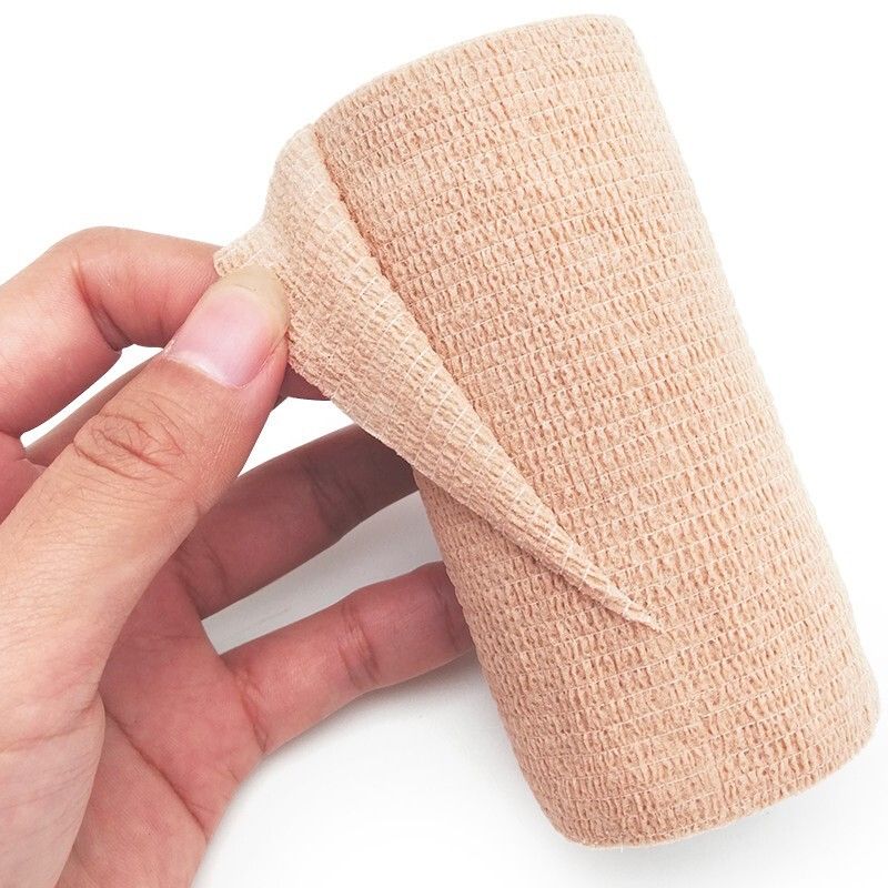 Hand holding an unrolled beige self-adhesive bandage