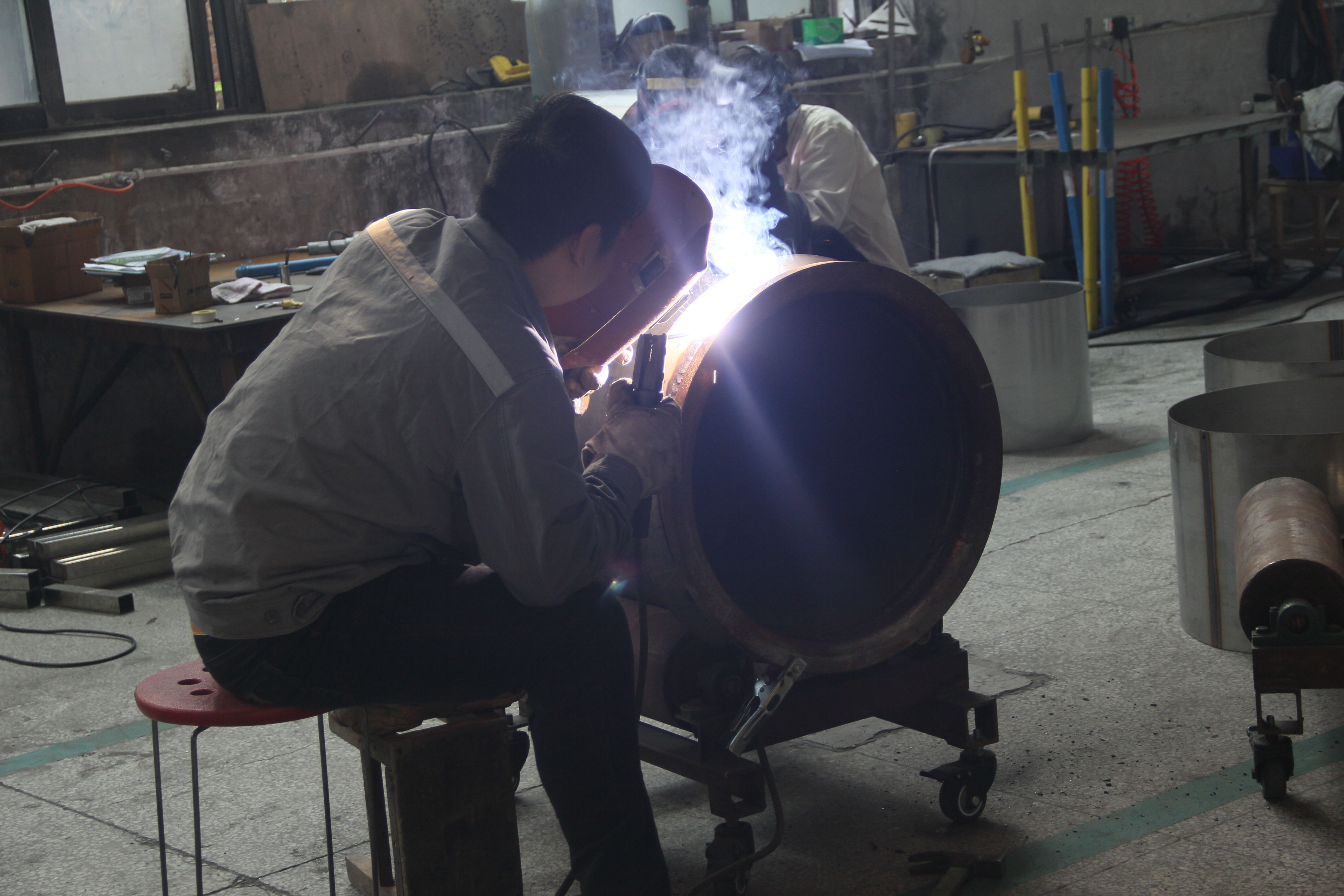 Worker welding reactor vessel in workshop