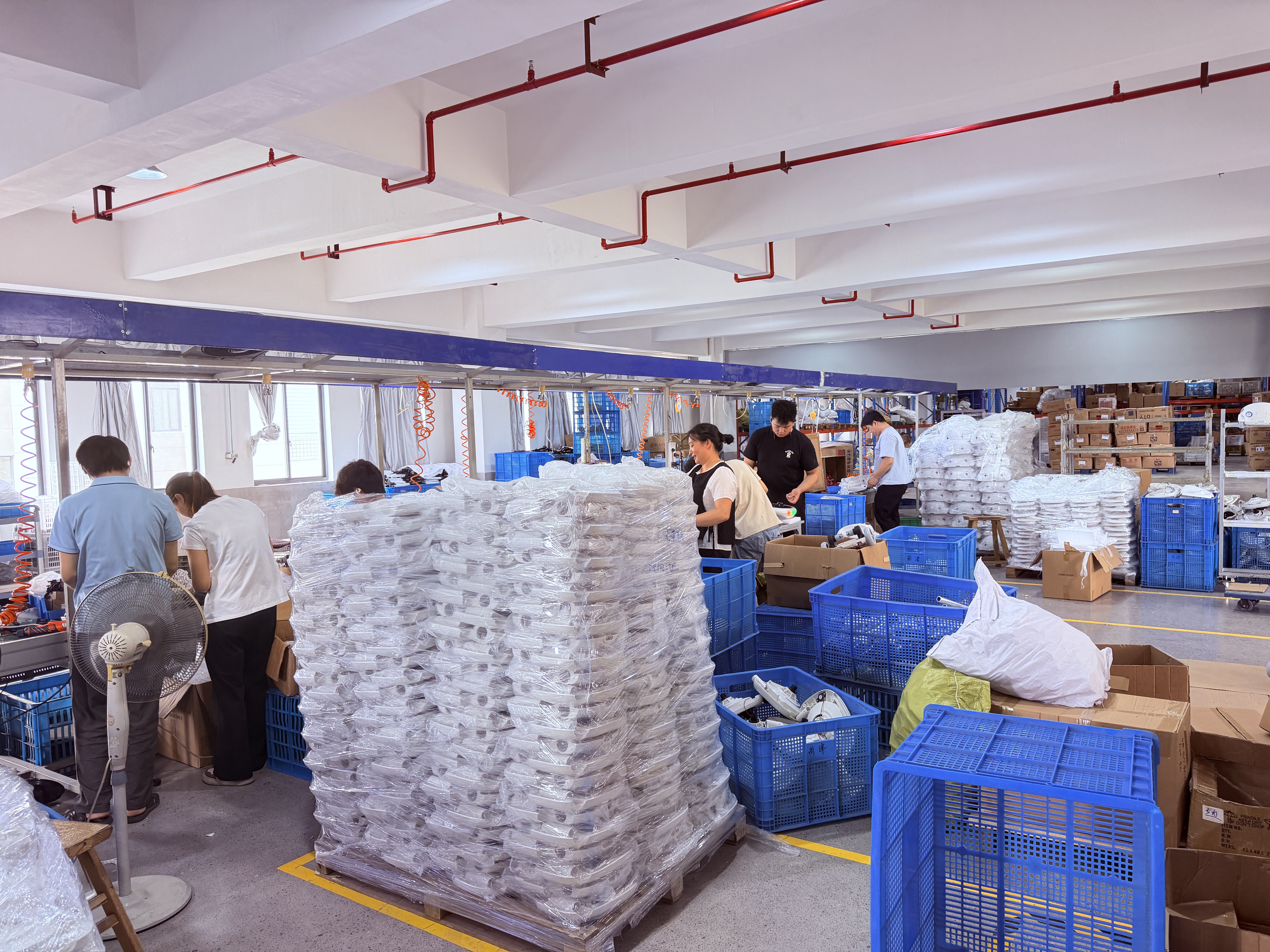 People working at benches with parts and blue crates in a workroom