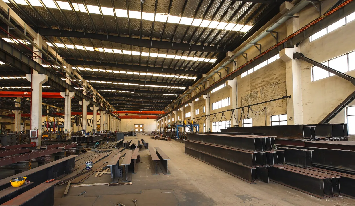 Interior view of the steel fabrication workshop with overhead cranes and steel beam stock