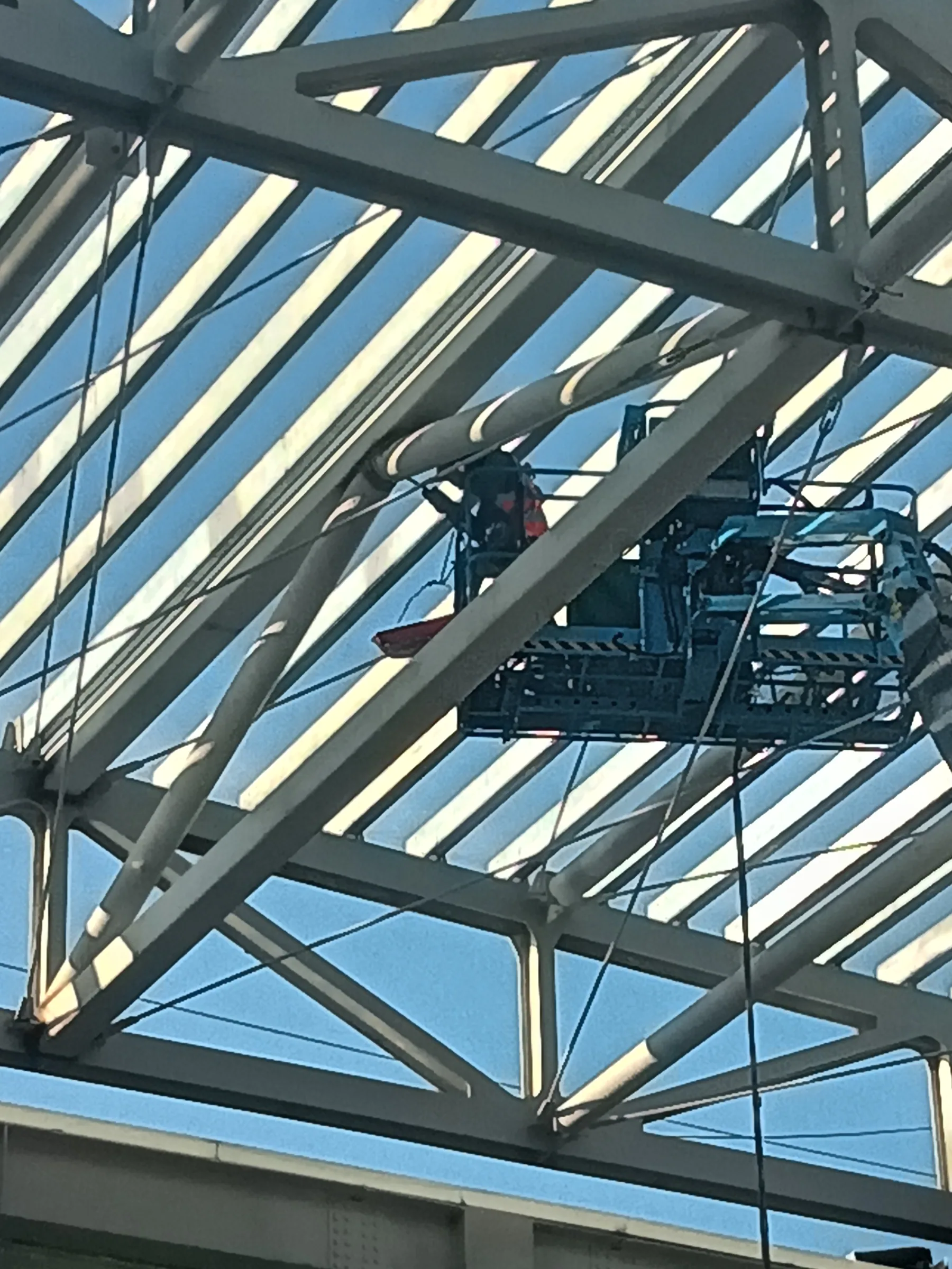 A worker on an aerial platform installing a steel roof truss above a Shanghai construction site