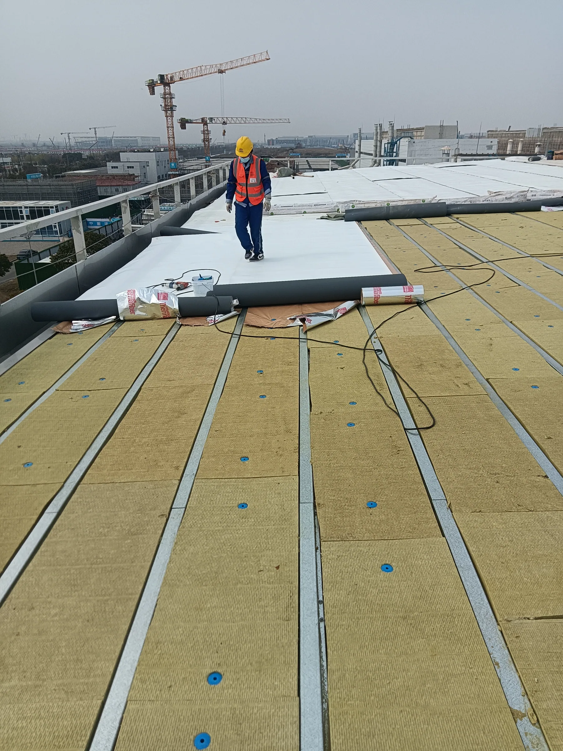 A worker installing roof insulation on a steel structure building under construction